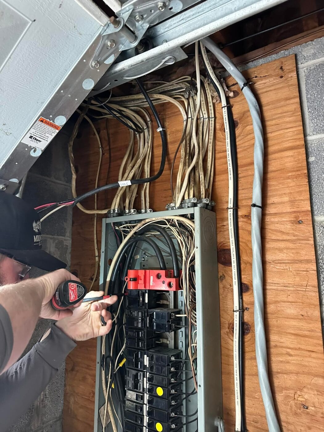 Person using a drill to work on an electrical circuit breaker panel with multiple wires on a wooden board.
