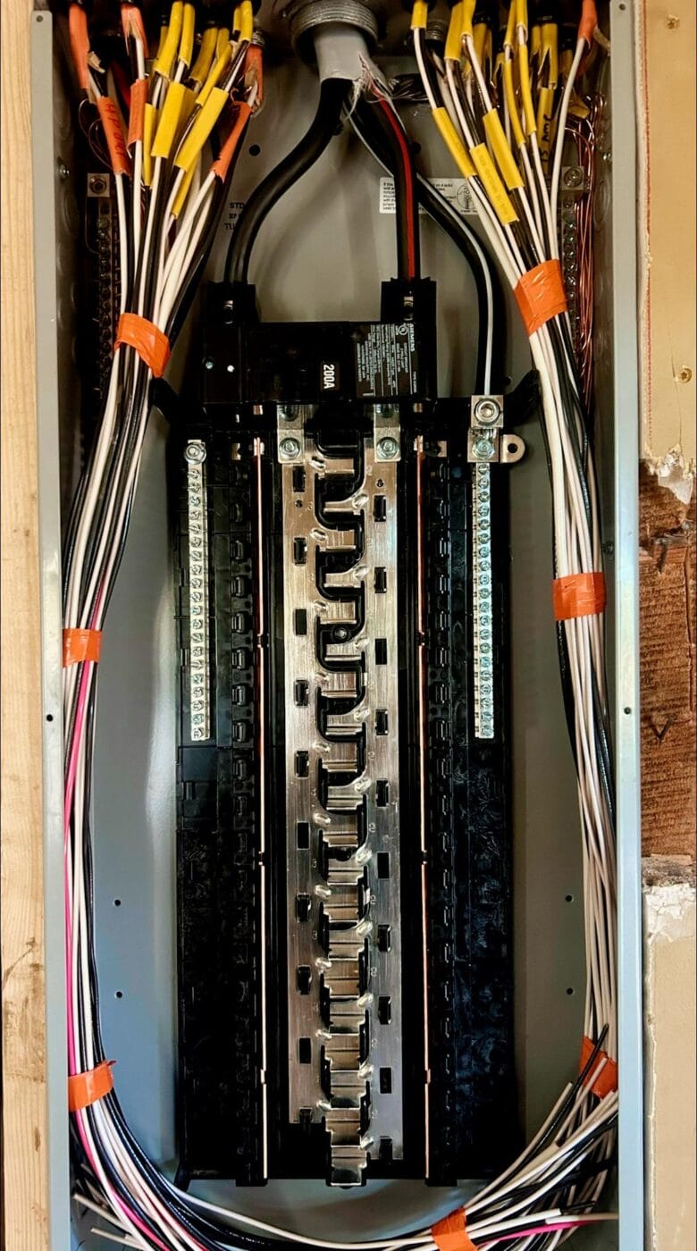 An open electrical panel with multiple organized wires secured by orange bands, revealing circuit breakers and connections.