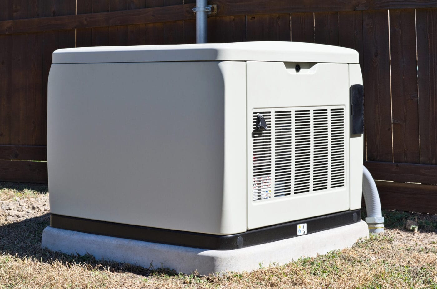 A standby generator installed on a concrete slab in a backyard, near a wooden fence.